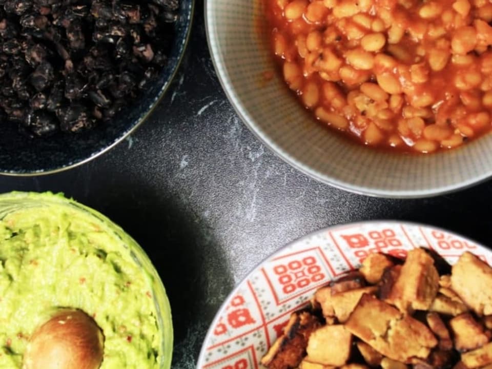 Vier Schälchen mit schwarzen und weissen Bohnen, Guacamole und Tofu.