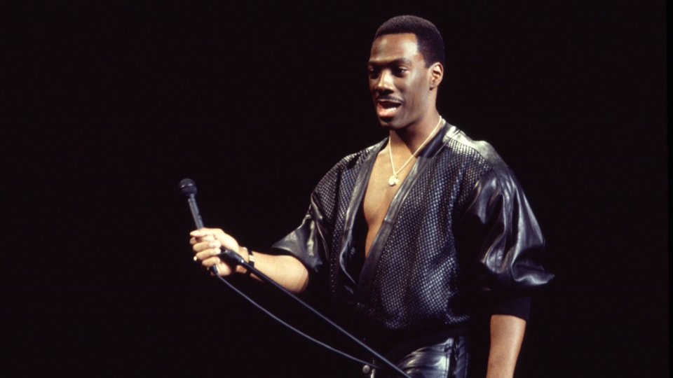 Eddie Murphy steht auf der Bühne und performt Stand-up-Comedy mit einem Mikorofon in der Hand.