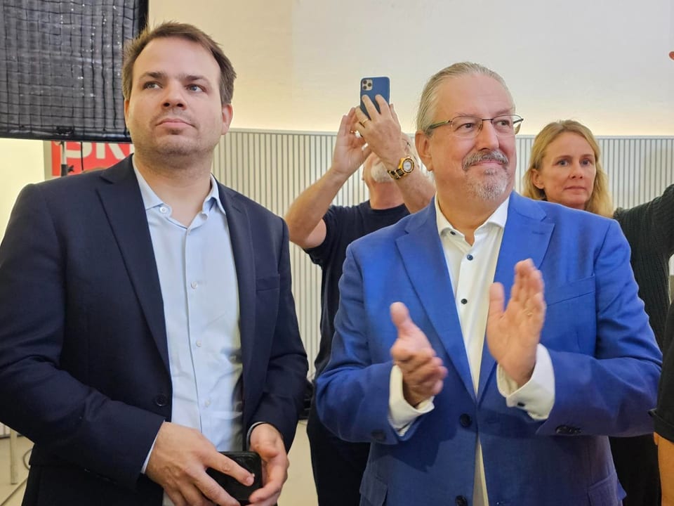 Dois homens de terno aplaudem. 