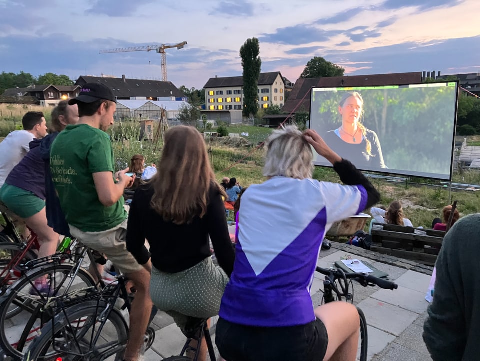 Fünf Kinobesucher strampeln auf dem Velo und schauen sich den Film auf der Leinwand an