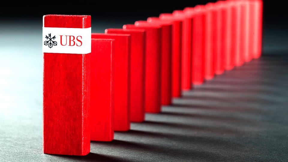 Rote Dominosteine verbildlichen die Schweizer Wirtschaft. Auf dem vordersten Stein prangt der Name der grössten Schweizer Bank, der UBS.