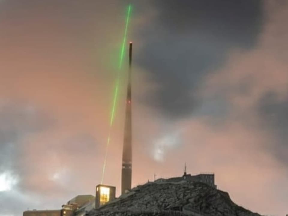 Der Laserstrahl richtet sich auf Wolken über dem Sendeturm auf dem Säntis
