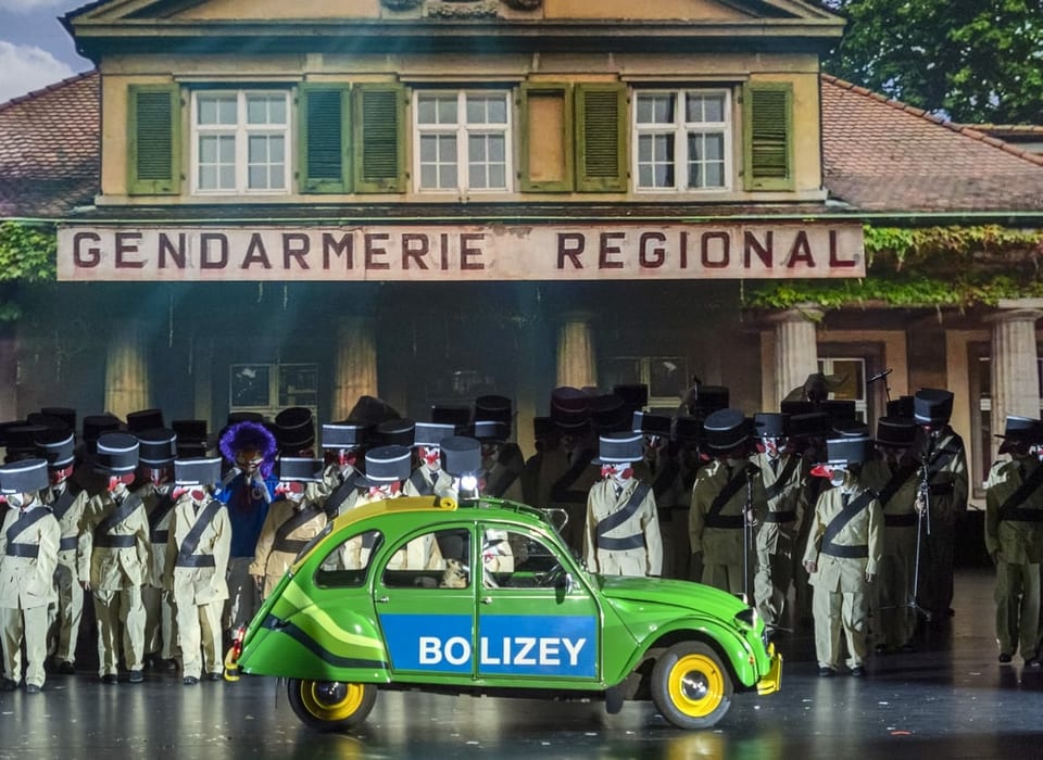 Ein grüner deux chevaux steht vor dem alten Polizeiposten am Wielandplatz. Dahinter stehen Gendarmen, also französische Polizisten.