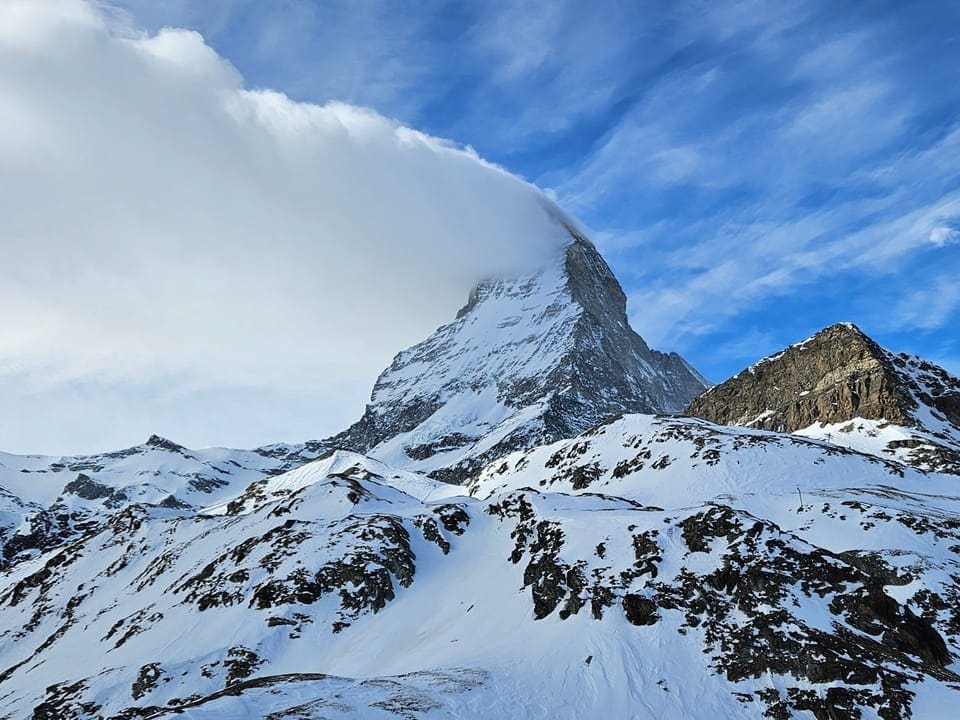 Matterhorn mit fahnenförmiger Wolke an der linken Flanke des Berges. Sonst ist der Himmel teils blau. 