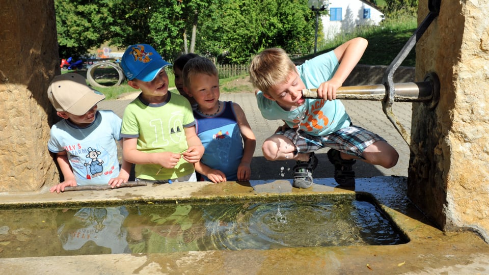 Kinder erfrischen sich am Dorfbrunnen in Bretzwil BL