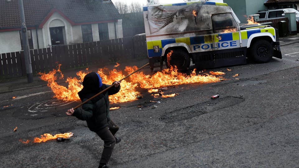 Ein Jugendlicher wirft eine Eisenstange auf einen brennenden Polizeiwagen