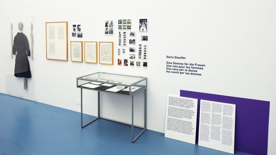 Blick in Museumsausstellung: Schaukasten mit Druckerzeugnissen, Bilder sowie Kleidungsstücke an der Wand