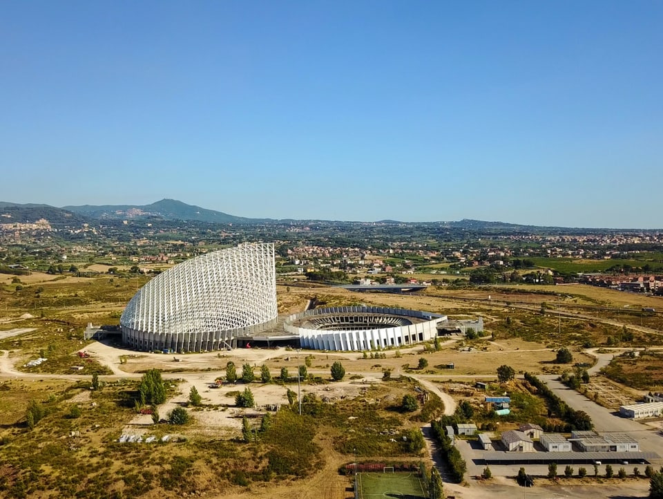 Segelartiges weisses Gebäude neben weissem unfertigen Stadium in verbrannter Landschaft