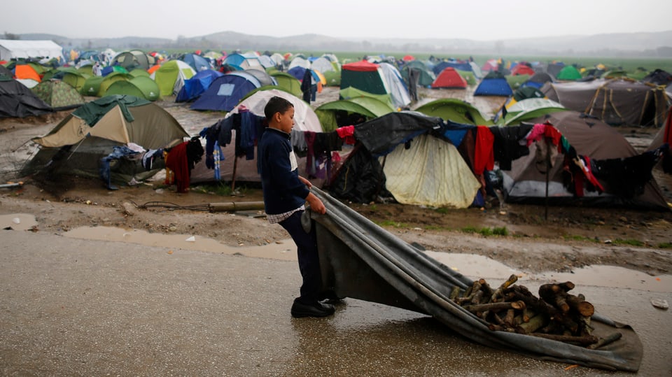 Ein Junge schleppt Holz zu seinem Zelt in Ideomeni. Derweil regnet es weiter. (reuters)