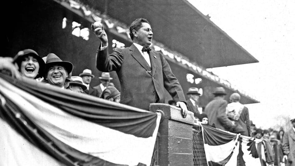 schwarz-weiss Foto eines Mannes auf Baseballtribüne, hält Baseball hoch.