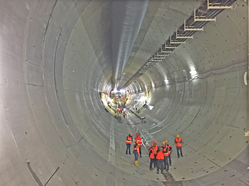 Tunnelröhre, rundherum Beton, darin ein paar klein wirkende Personen in orangen Leuchtwesten