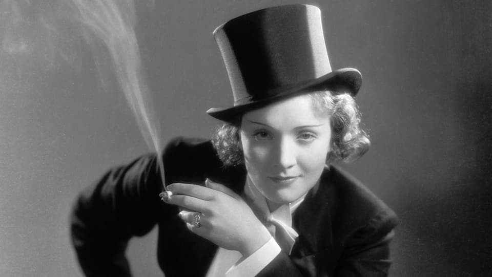 Marlene Dietrich im Anzug mit Zylinder und Zigarette.