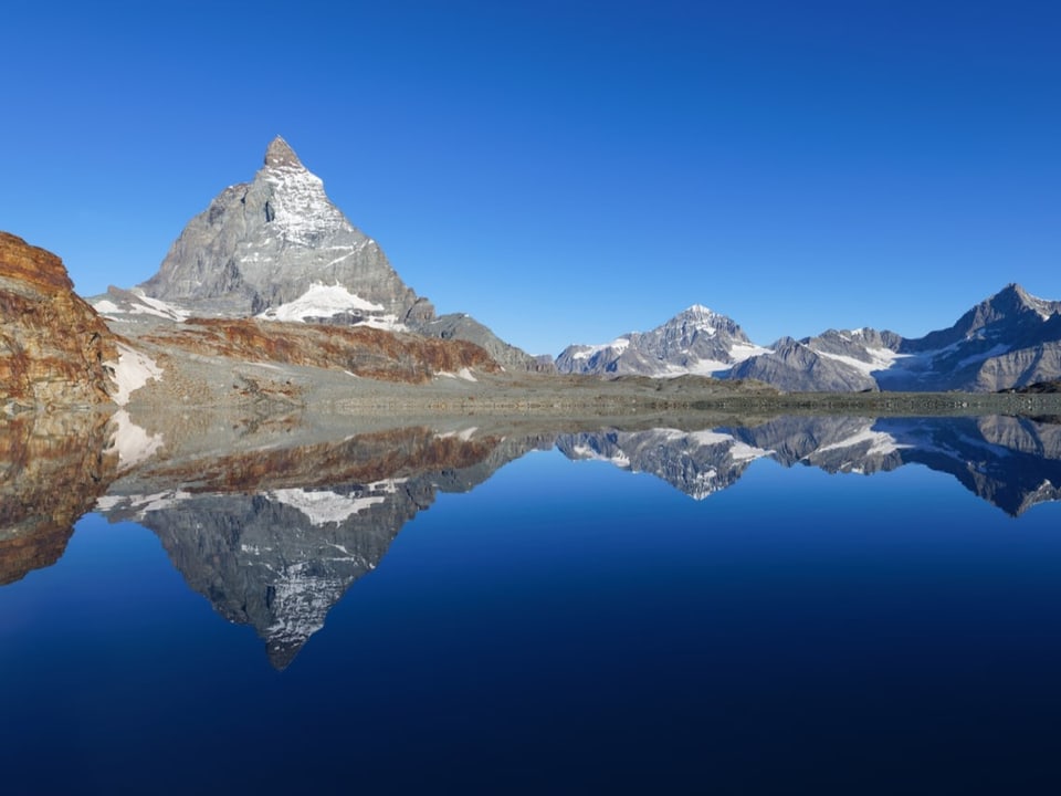 Stahlblauer Himmel mit Bergen, die sich in einem Bergsee spiegeln. 