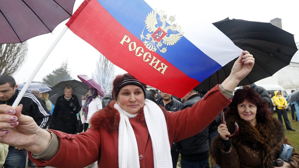 Pro-russische Demonstration auf der Krim, eine Frau hält eine Russland-Fahne in die Kamera.