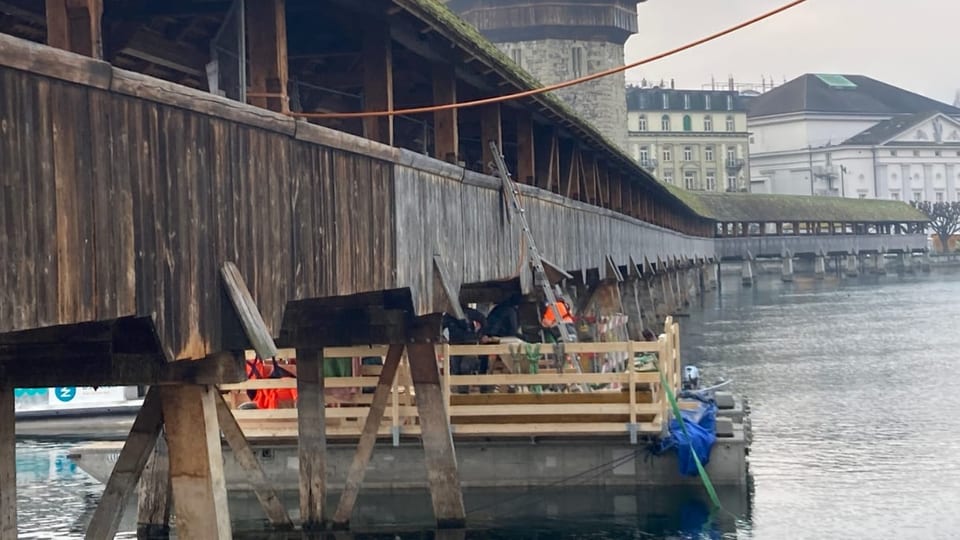 Unter der Holzbrücke schwimmt ein viereckiges kleines, flaches Schiff.