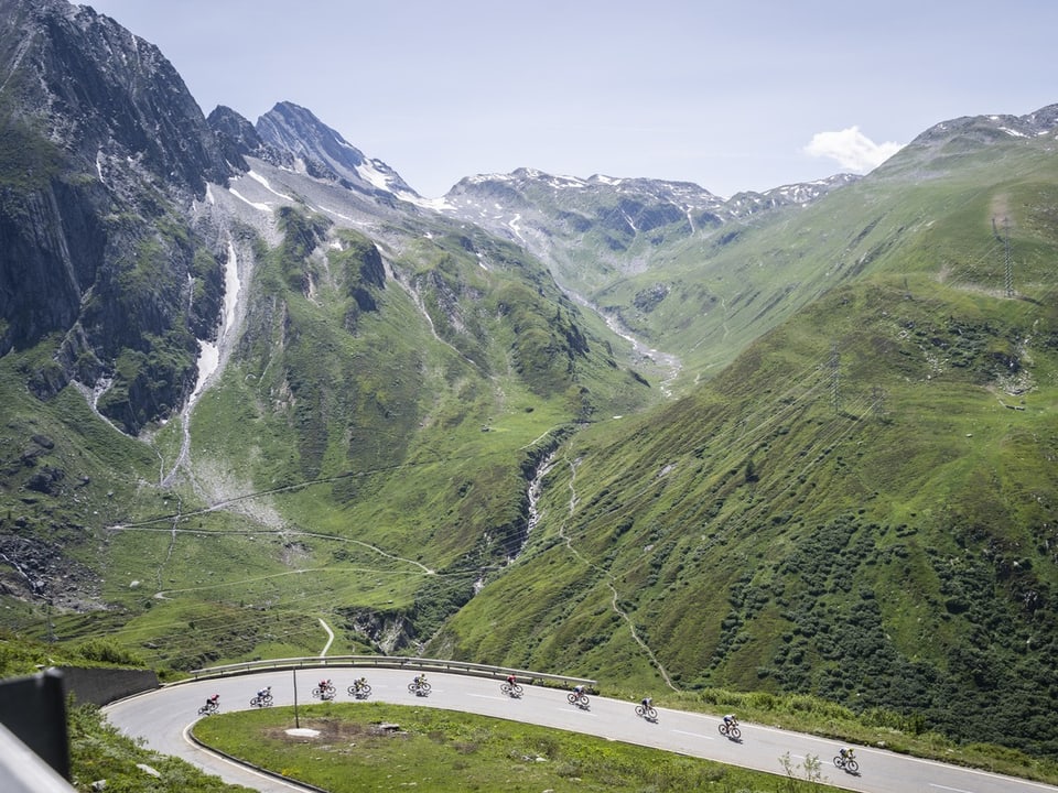 Bergstrasse mit Radfahrern in den Alpen, grüne Landschaft mit Wasserfall.