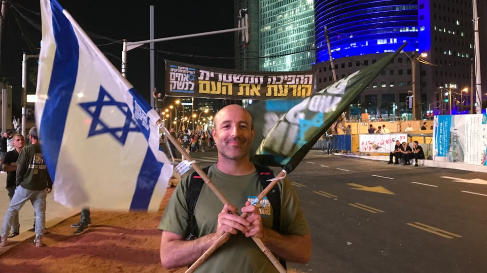 Golov mit zwei Israel-Fahnen auf einer nächtlichen Strasse, er lächelt.