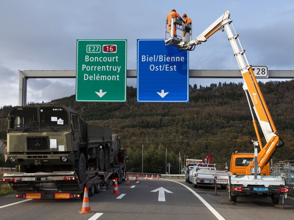 Arbeiter in einer Hebebühne montieren Verkehrsschilder über einer Autobahn. Auf dem Schild steht Biel/Bienne.
