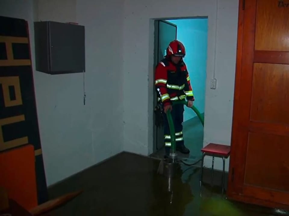 Ein Feuerwehrmann pumpt Wasser aus dem Untergeschoss einer Wohnung. Der Boden ist knöcheltief mit Wasser bedeckt.