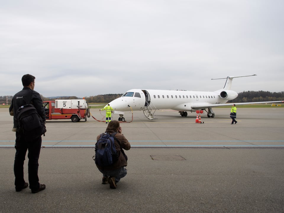Zwei Männer fotografieren einen Businessjet. Sie stehen fast auf dem Flugfeld.