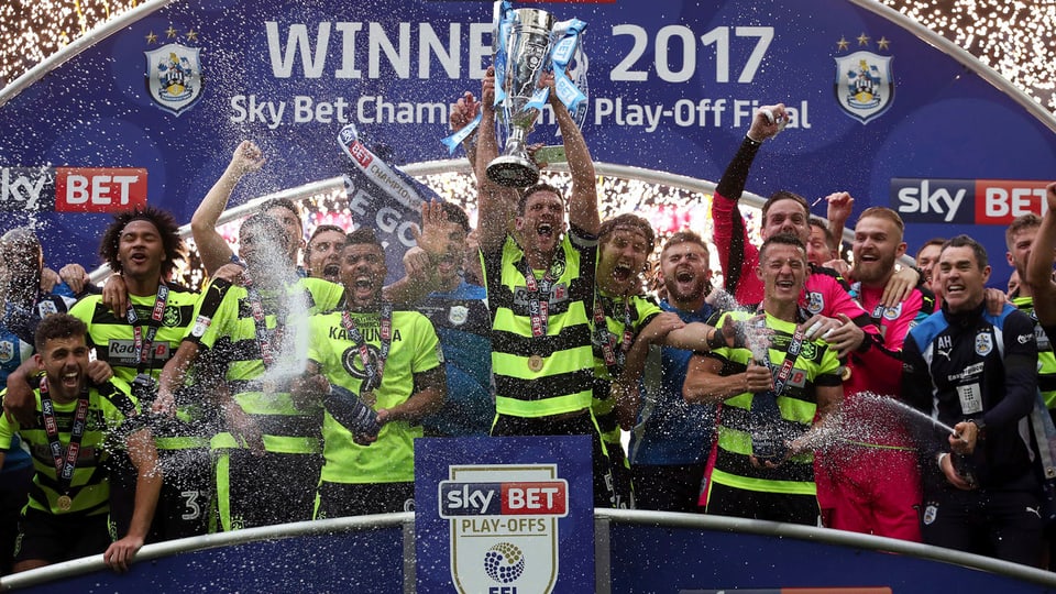 Die Spieler von Huddersfield Town stemmen einen Pokal in die Luft. Es regnet Konfetti.