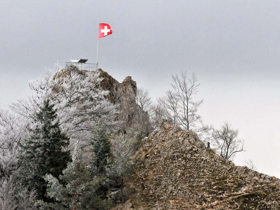 Auf dem Juragipfel weht eine Schweizer Fahne. Links am Hang ist es weiss. Rechts davon ist der Boden grün.