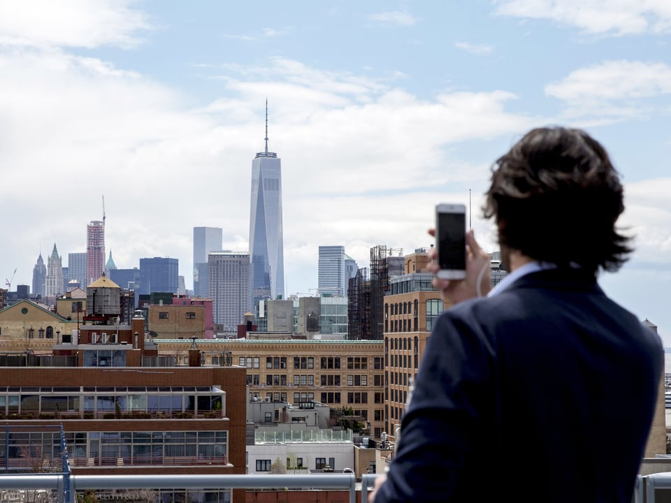 Ein Mann steht am Fenster und fotografiert die Aussicht über Manhattan. 