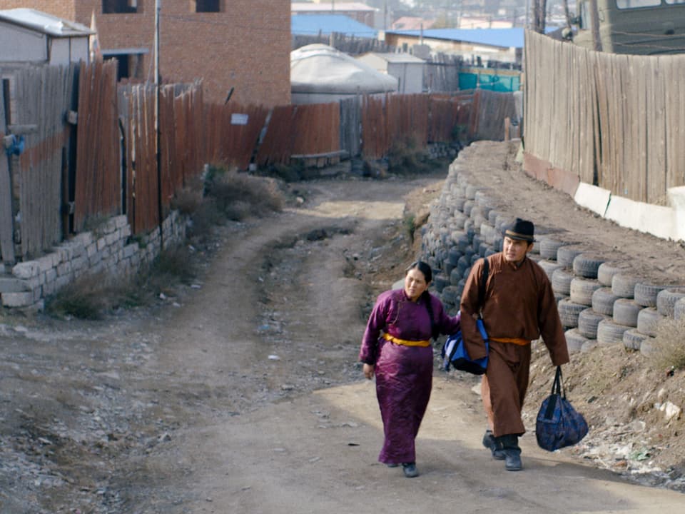 Zwei Personen in traditionellen mongolischen Kleidern gehen durch eine Stadt.