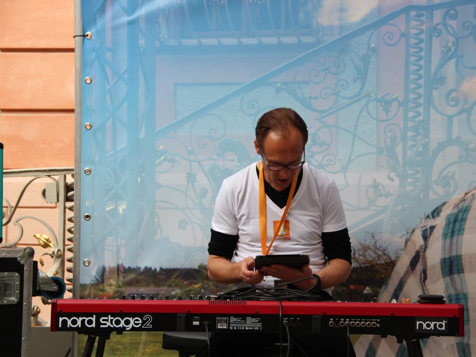 Christian Zeugin sitzt hinter seinem Piano und schaut auf sein Tabletcomputer.