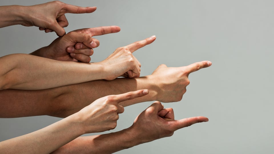 Ein Dutzend ausgestreckter Arme zeigen mit erhobenem Zeigefinger nach rechts.