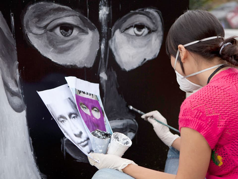 Eine Frau übermalt das Porträt von Putin mit schwarzer Farbe.