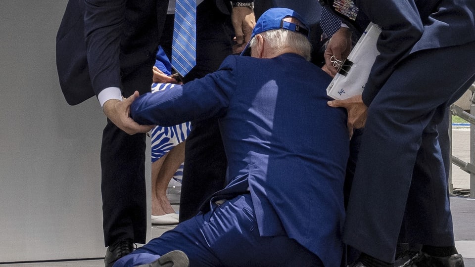 US-Präsident Biden liegt am Boden, während ihm andere Leute versuchen aufzuhelfen.