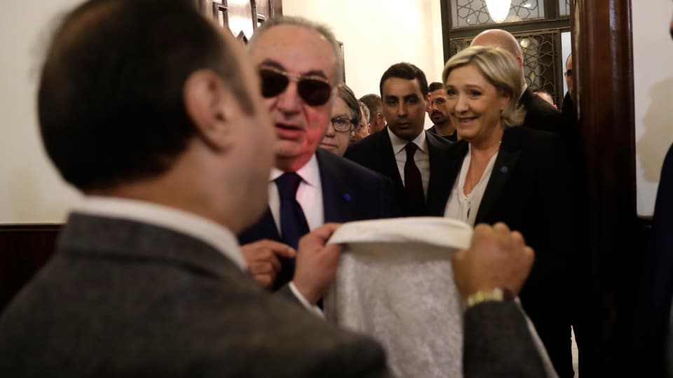 Le Pen in Beirut, vor ihr hält ein Mann ein Kopftuch in die Höhe. 