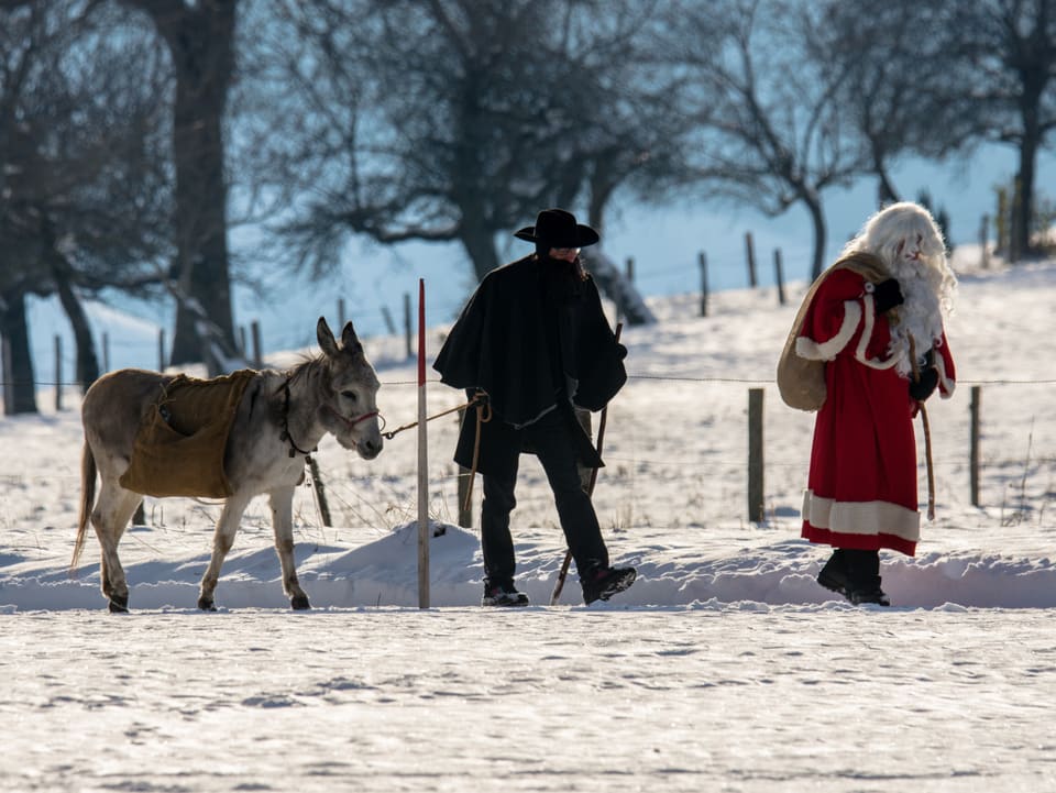 Der Samichlaus mit Esel und Schmutzli auf dem Weg durch die verschneite Landschaft zu den Kindern im Wald in Rüeggisberg BE.