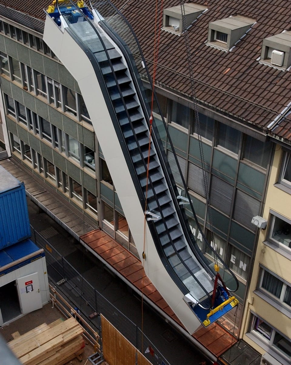 Ein Rolltreppe wird an Kranseil transportiert