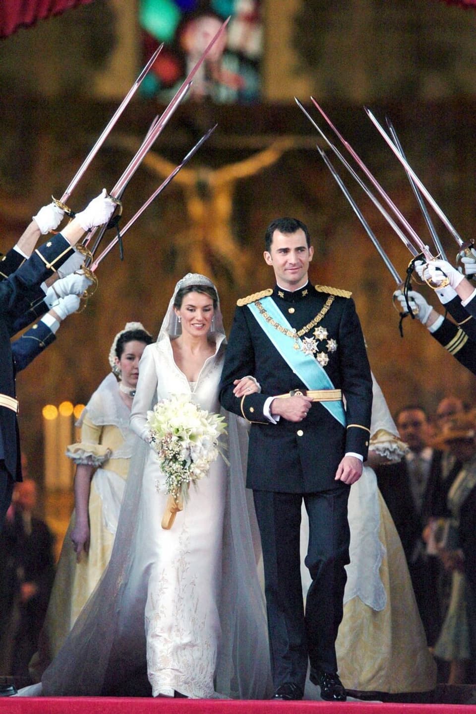 Felipe in Uniform und Letizia im Brautkleid schreiten unter hochgehaltenen Schwerten durch.