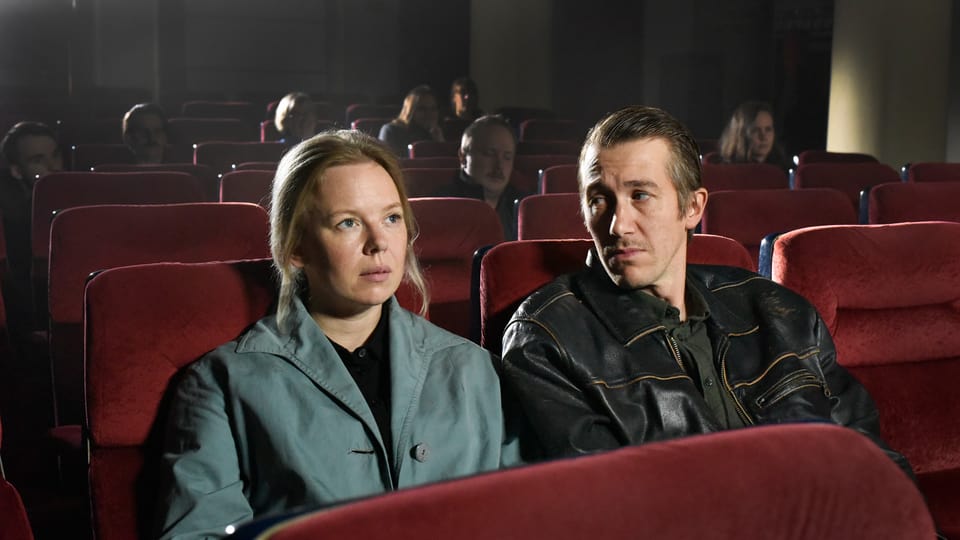 Szene im Kino, rote Sessel, eine Frau und ein Mann sitzen nebeneinander, der Mann sieht die Frau an