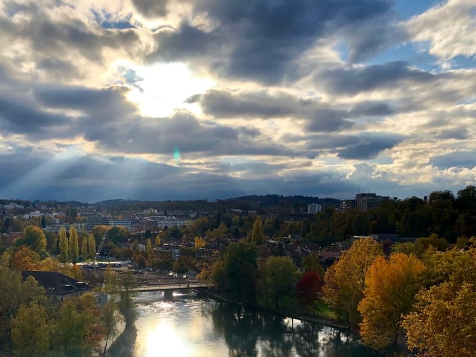 Stadt mit Fluss mit Wolken und etwas Sonne mit farbigen Bäumen.