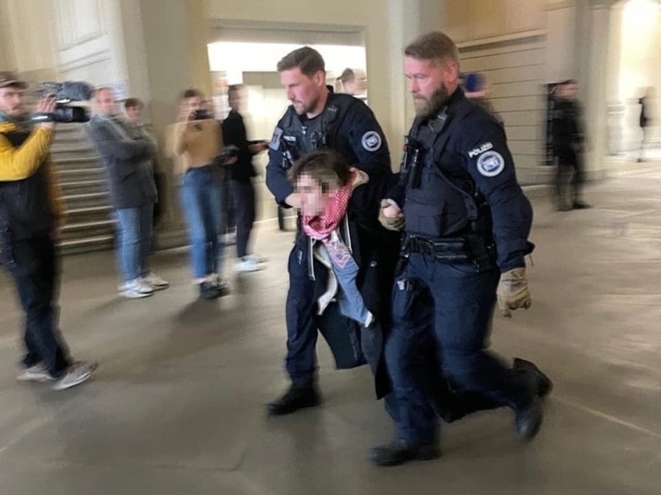 Polizisten führen einen protestierenden Mann in einem öffentlichen Gebäude ab.