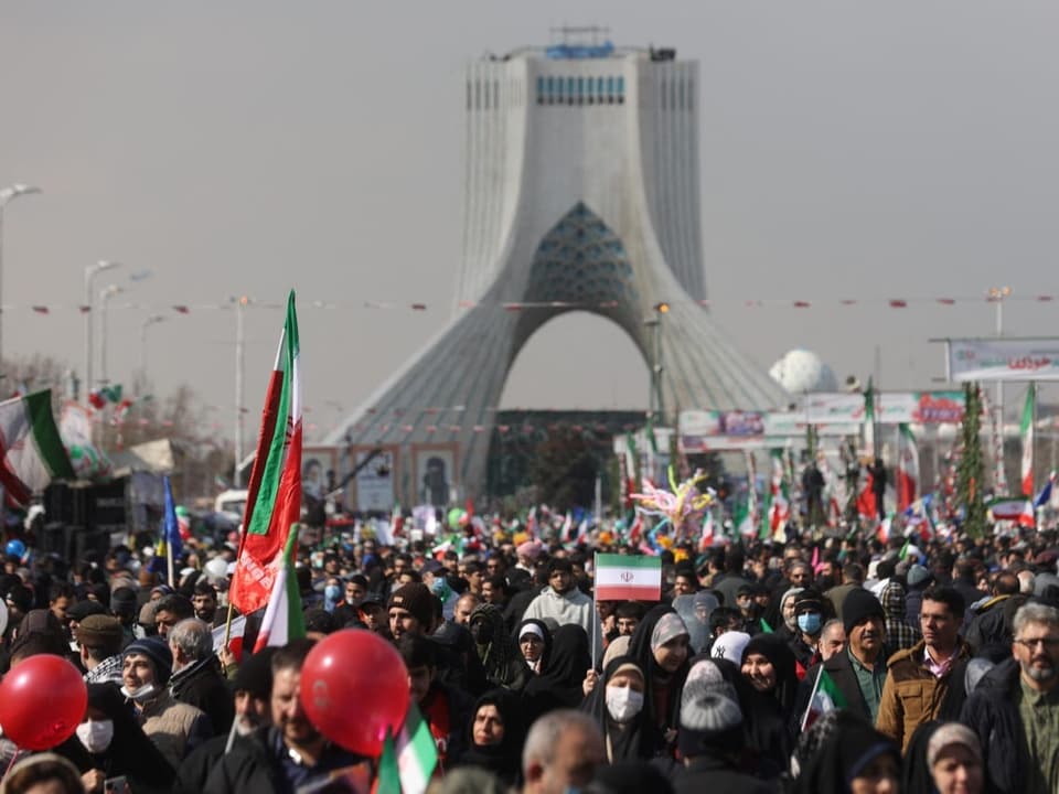 Viele Menschen gehen auf einer Strasse. Sie halten teilweise Iran-Flaggen in die Luft.