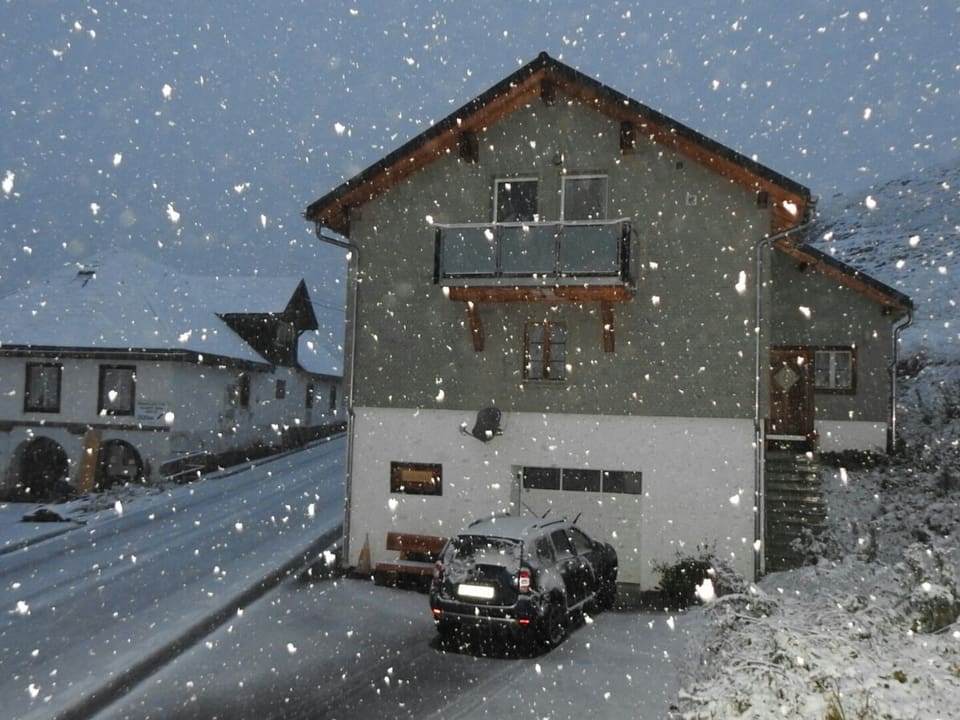 Haus an einer Passstrasse mit etwas Schnee auf der Strasse und Schneeflocken in der Luft. 