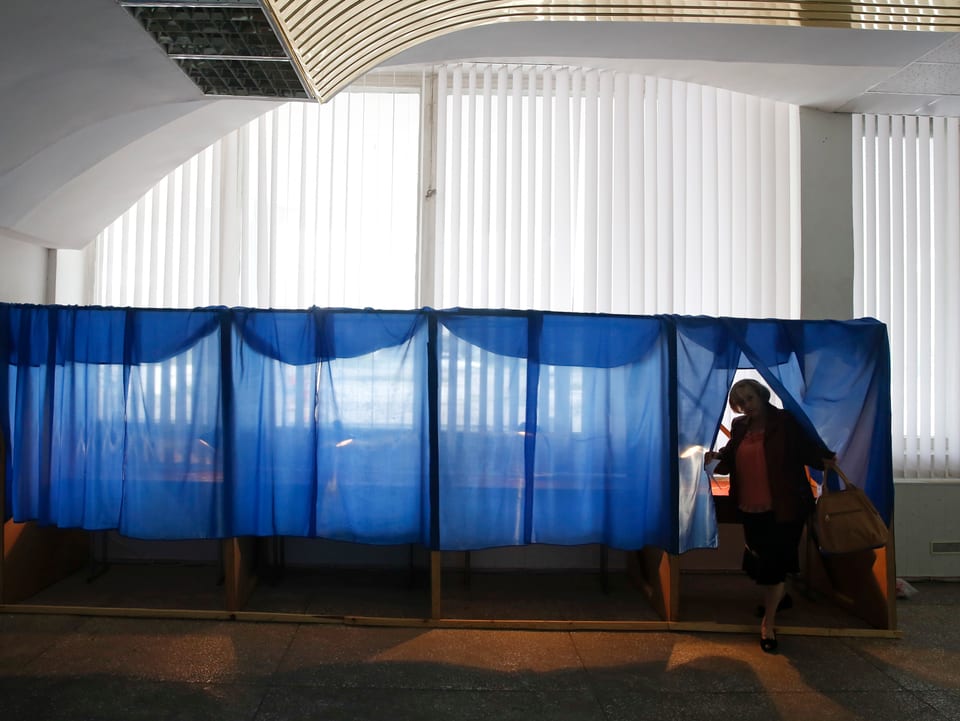 Eine Frau kommt in einem Wahllokal hinter einem Vorhang hervor. Sie ist die einzige im Raum.