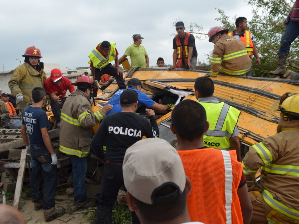 Feuerwehrleute inspizieren einen Linienbus, der vom Sturm fast komplett zerstört worden ist.
