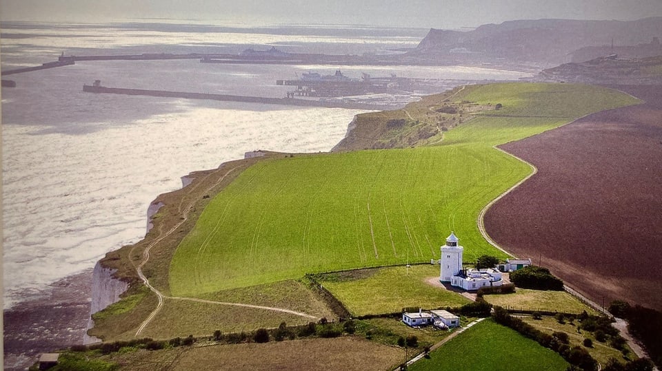 Leuchtturm inmitten grüner und brauner Felder an der schroffen Küste. Bild von oben
