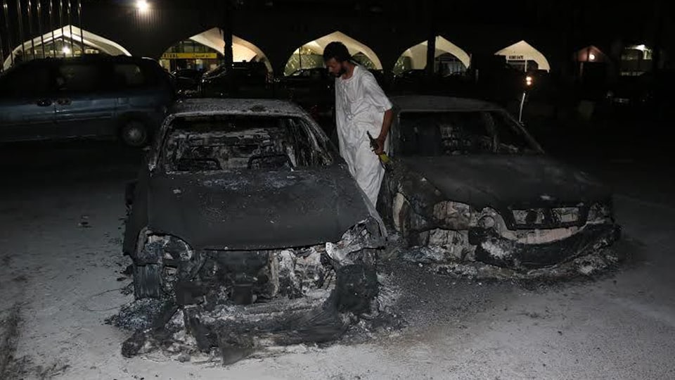 Ein bewaffneter Mann in weissem Kleid besichtigt ausgebrannte Autowracks.