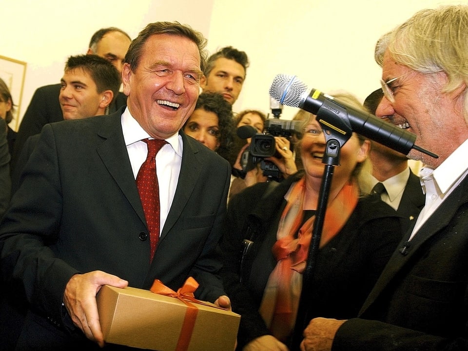 Schröder hat eine Schachtel Zigarren erhalten und lacht in die Kamera, zusammen mit Schang Hutter.