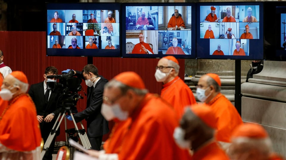 Kardinäle, im HIntergrund eine Videowand mit Bildern von anderen Kardinälen.