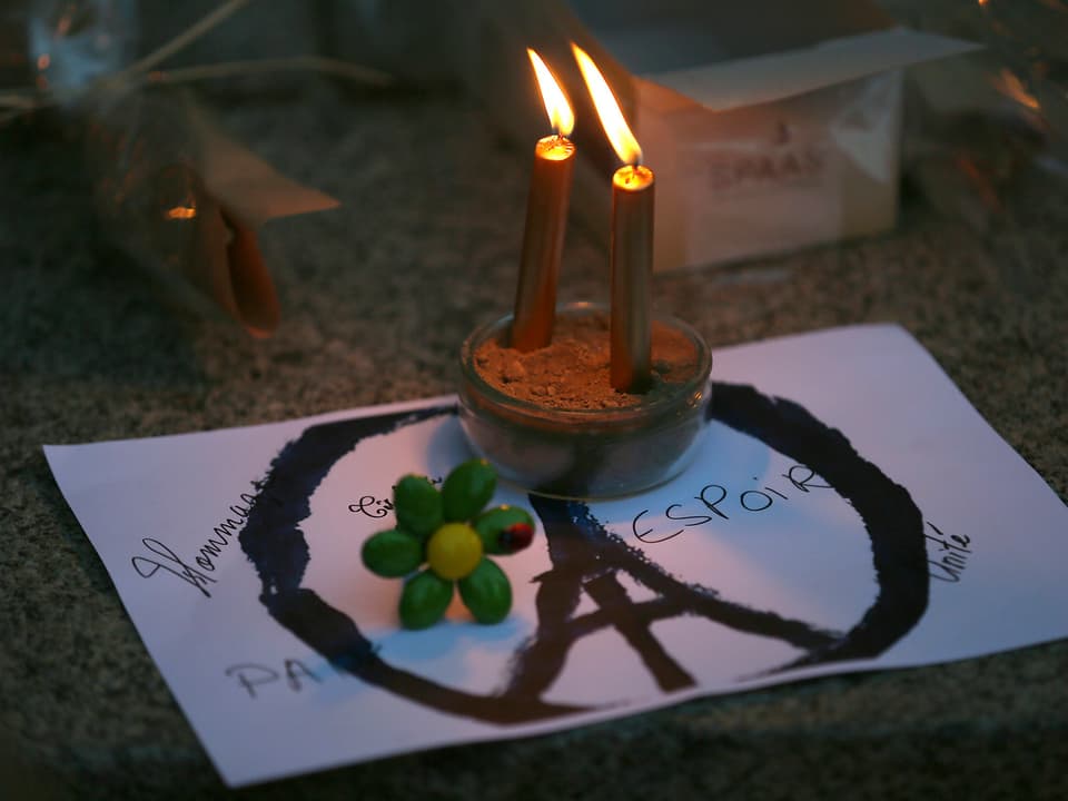 Das angepasste Peacezeichen auf dem Boden, darüber stehen Kerzen. 