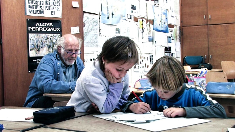 Lehrer Gilbert Hirschi im Hintergrund, zwei Schüler zeichnen im Vordergrund.