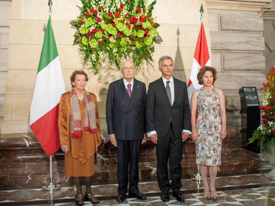 Vier Personen in einer Reihe vor den Flaggen der Schweiz und Italiens stehend..